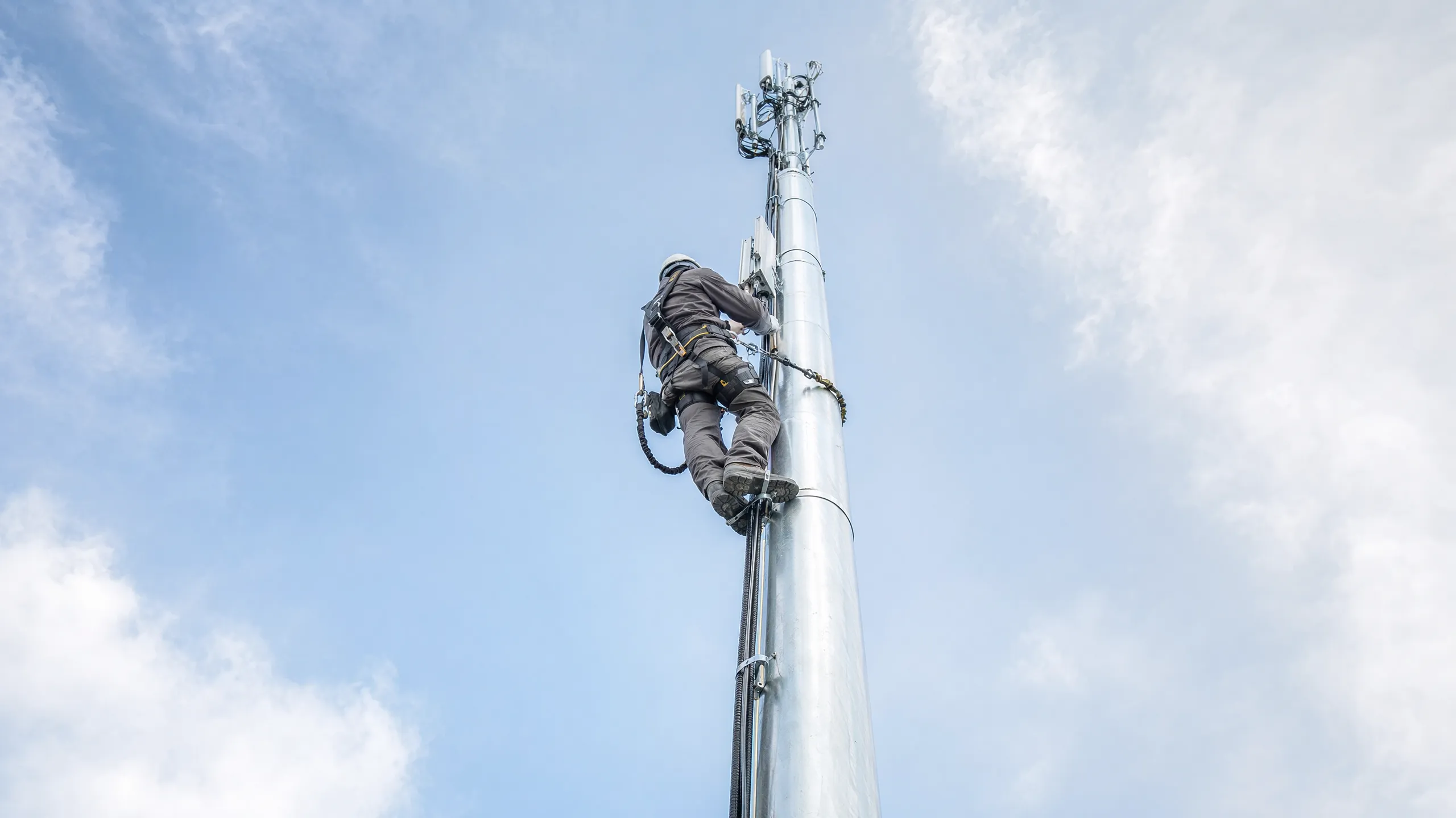 Technician inspecting attachments on a slim monopole from below